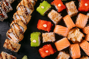 Maki and rolls with tuna, salmon, shrimp, crab, red and green caviar. served with wasabi and ginger on black background. Top view of assorted sushi. Japanese food. professional macro photo. 