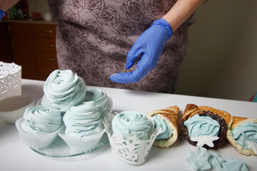 Woman in rubber gloves makes marshmallows. Nearby is a zephyr in a waffle cone. Dessert lies on the table surface.