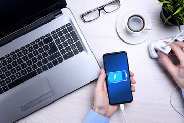 Businessman at the desk puts a smartphone, mobile phone to charge. Laptop, cup of coffee, glasses....
