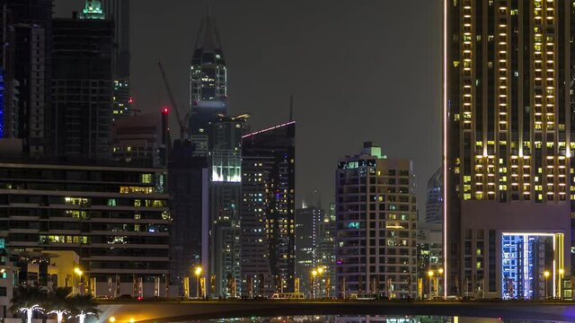 Promenade and bridge with traffic over canal in Dubai Marina timelapse at night, UAE. View from bridge with palms, boats and towers. District with artificial canal and illuminated skyscrapers