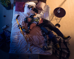 Flying. Top view of young professional hockey player sleeping at his bedroom in sportwear with equipment. Loving his sport, workaholic, playing match even if resting. Action, motion, humor.