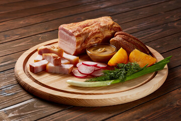 Ham garnished with vegetables, fruits and herbs with sauces and bread on a wooden plate on a dark wooden table.