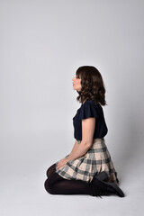 Full length portrait of pretty brunette woman wearing tartan skirt and blouse.  Sitting pose on the...