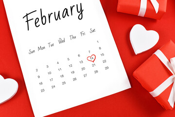 Close up of February calendar sheet with Valentine's Day on the 14th marked with red heart surrounded by gift boxes and heart on red background