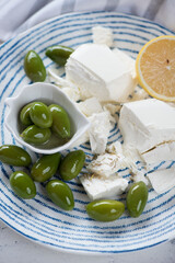Giant green olives, blocks of feta cheese and lemon on a blue and white plate, vertical shot, closeup