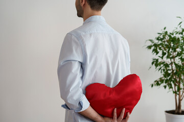 A man holds a soft red heart toy behind his back. The face is not visible. Valentines day.