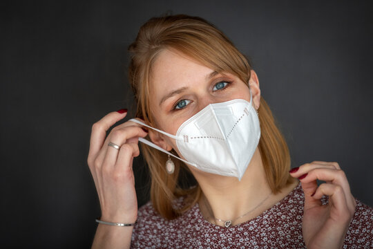 Junge rotblonde Frau zieht sich eine FFP2 Schutzmaske auf gegen das Coronavirus - Querformat vor dunkelgrauem Hintergrund isoliert