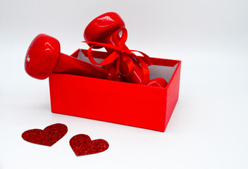 Two red dumbbells with a ribbon bow in an open red box and two hearts on a white background. Concept of Valentines day, healthy lifestyle, giving gifts, love of sports.
