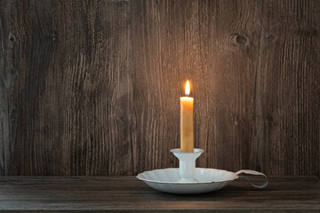 burning candle in a candlestick on a wooden background