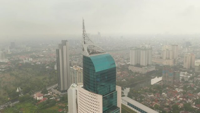Close up aerial dolly shot of the top of Wisma 46 skyscraper in Jakarta, Indonesia on a cloudy day