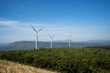 Wind turbines on green mountain over a cloudy blue sky.