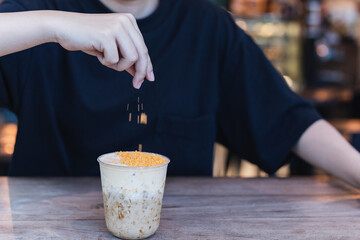 Barista sprinkles salted egg yolk powder on iced chocolate in cafe.