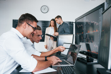 Attention to details. Team of stockbrokers works in modern office with many display screens
