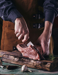 A guy in a leather apron is slicing raw meat. The butcher cuts the pork ribs. Meat with bone on a...