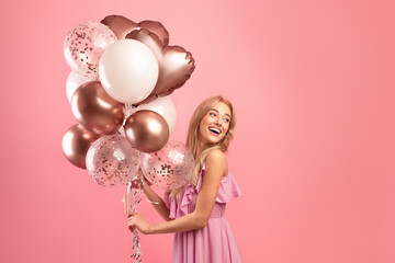 Party time. Charming blonde woman in stylish dress holding birthday balloons over pink studio...
