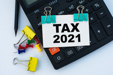 TAX 2021 - words on a white sheet with clips on a white background with a calculator, buttons and yellow stationery clips