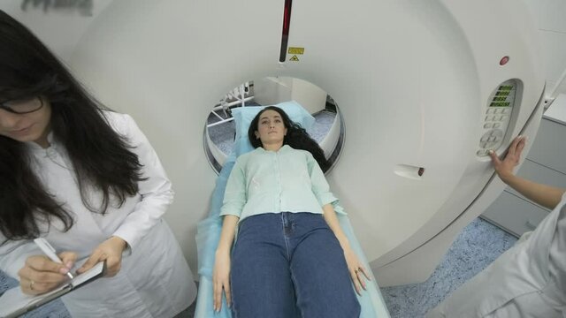 Female patient is undergoing CT or MRI scan under supervision of two qualified radiologists in modern medical clinic. Patient lying on a CT or MRI scan bed, moving inside the machine.