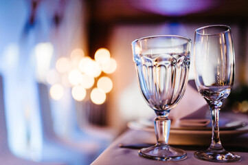 Close up picture of empty glasses in restaurant and cutlery. Silverware or flatware on plates, glasses for champagne and wine glasses. Reflection, bokeh and bright light.