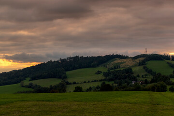 Obraz premium Sunset over mountains and hills with colorful clouds on the horizon that spill from side to side in orange.