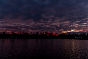 The water surface of the lake during a colorful sunset with the reflection of the surrounding tree on the water surface.