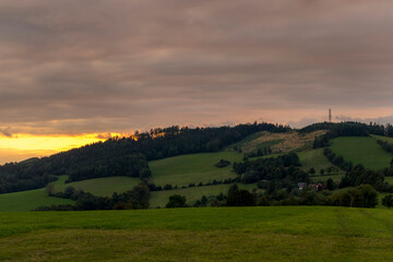Fototapeta premium Sunset over mountains and hills with colorful clouds on the horizon that spill from side to side in orange.