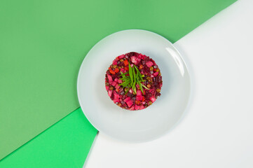 Directly above of Russian vinaigrette vegetable salad of beetroot. Traditional salad with oil and vinegar served with spring onion scallions on plate on colorful green background
