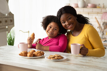 African mother and little daughter having a bite in kitchen together