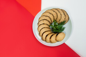 Stuffed carp fish. Jewish traditional gefilte fish slices served with fresh green herbs - dill and parsley on red and white abstract background. Holiday homemade fish dish
