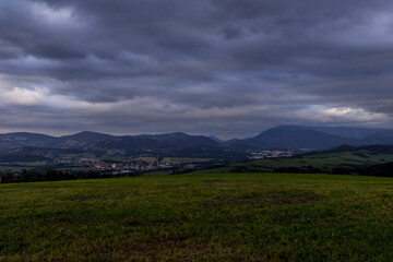 Obraz premium Sunset over mountains and hills with colorful clouds on the horizon that spill from side to side in orange.