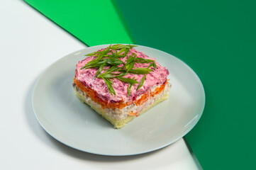 Side view of Russian traditional Shuba salad with layers of vegetables and fish fillet. Herring under the fur coat beetroot salad served with spring onion scallions on colorful green background
