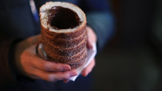 Close-up of a baked bun with sugar in the hands of a tourist on the street in the evening city. Traditional food in the Prague city. Camera movement, soft focus.