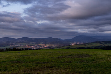 Sunset over mountains and hills with colorful clouds on the horizon that spill from side to side in orange.