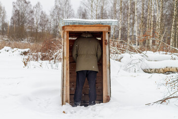 Wooden toilet without a door on the street in winter. A man in the toilet.