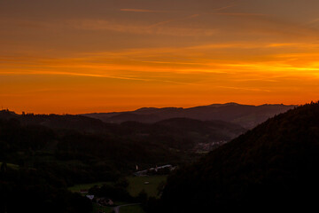Setting sun in a valley landscape flooded with orange gold color moving beyond the horizon overlooking the mountains and surrounding hills.