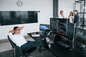 Man sits on chair and takes break. Team of stockbrokers works in modern office with many display...
