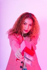 Asian curly hair woman in pink jacket with red money gun on neon light background.