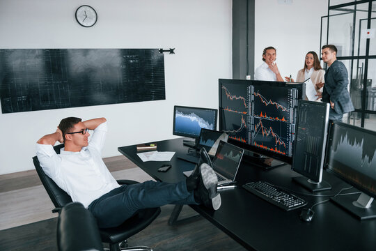 Man sits on chair and takes break. Team of stockbrokers works in modern office with many display screens