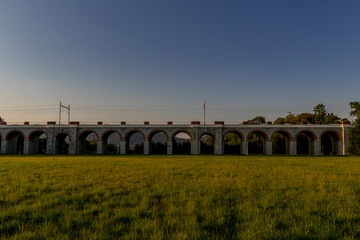 Railway viaduct with passing trains and cars in an underpass during a sunny day with moving clouds in the sky.