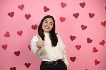 Young beautiful woman over pink background with harts smiling friendly offering handshake as greeting and welcoming