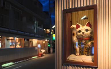 Early evening view of a maneki-neko, a Japanese symbol of good fortune, in a display case at the front entrance of a store (translation: collar means "luck", coins mean "ten million gold pieces")