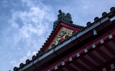 Late afternoon view looking up at a decorative part of the eave of a roof of a Japanese temple under a partly cloudy sky