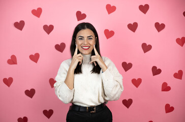 Young beautiful woman over pink background smiling confident showing and pointing with fingers teeth and mouth with harts