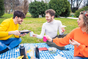 Naklejka na ściany i meble Three caucasian friends having picnic in a park