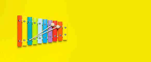 Multicolored wooden xylophone and shock sticks on bright yellow background flat lay top view copy...