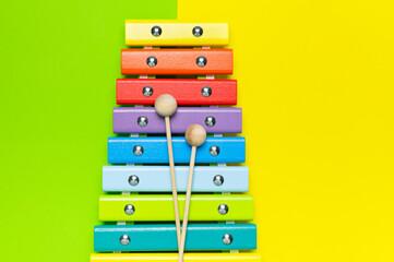 Multicolored wooden xylophone, shock sticks on yellow and green background flat lay top view copy...
