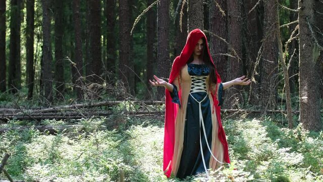 A girl in a red cloak in the forest among the trees. Moves his hands. Does the magic of hand movements. The Forest Witch