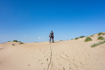 Man walking with bicycle on a sand dune with blue sky, Platja del Fangar,  Spain