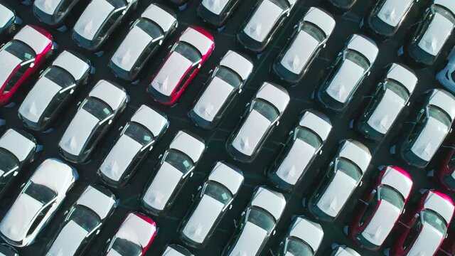 Aerial top down view of new cars parked in car parking lot. Car dealer parking lot full of new automobiles. New cars lined up for import and export business.