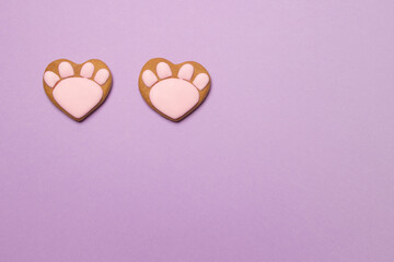 close up of valentine cookies in form of cat paws on purple colored paper background with copyspace