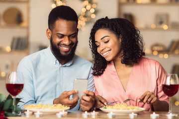 Smiling black couple using smartphone during romantic dinner